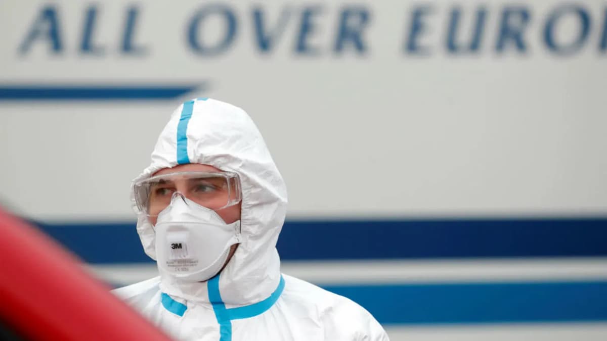 Une personne en combinaison de protection intégrale et masque FFP2 devant un autocar.