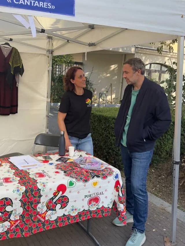 Sous une tente, deux personnes discutent devant une table couverte d’une nappe portugaise.