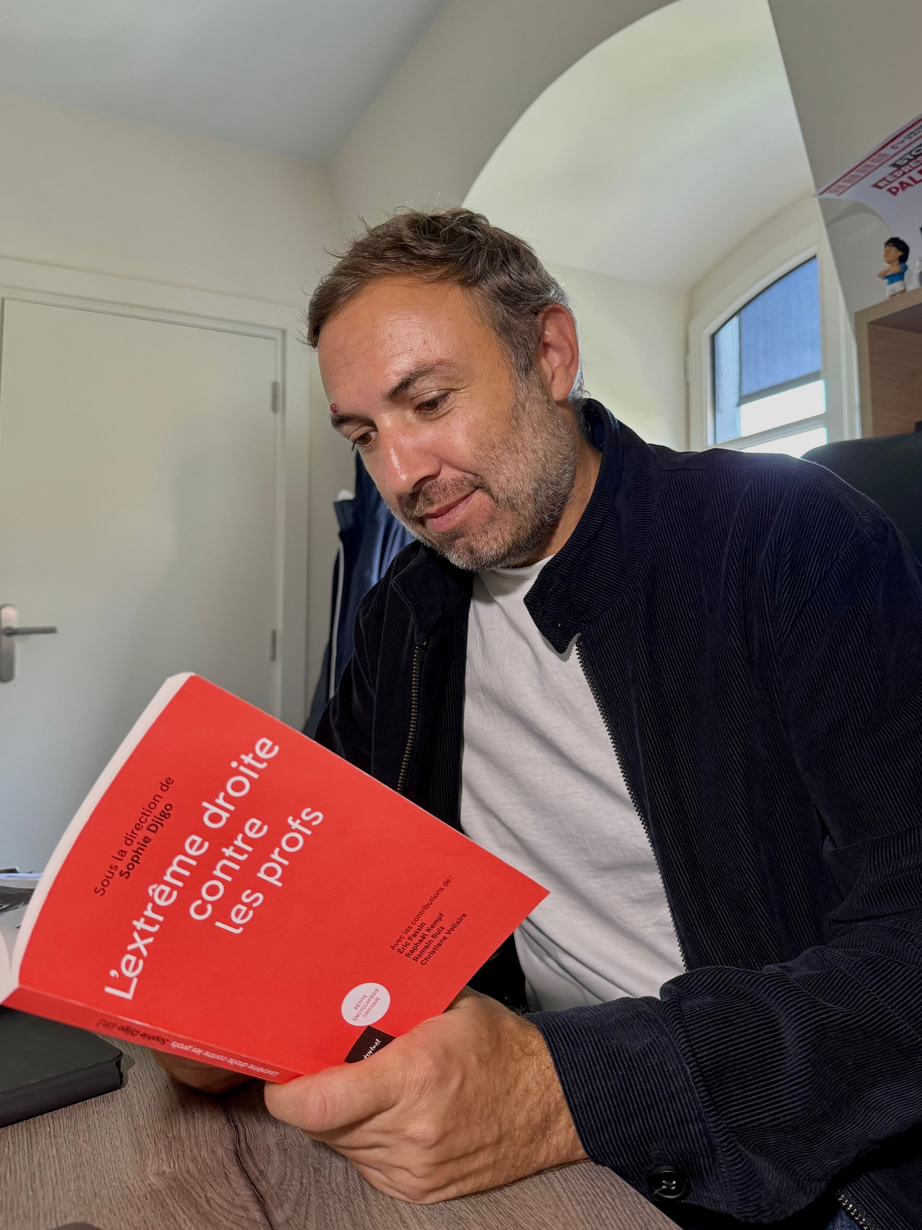 Un homme lit le livre « L’extrême droite contre les profs », assis dans un bureau.