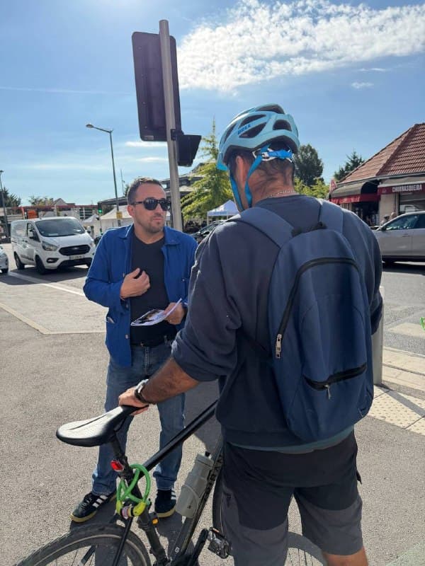 Un militant en veste bleue parle à un cycliste casqué à un carrefour.