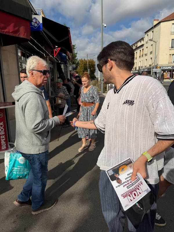 Un militant tend un tract à un passant devant des commerces.