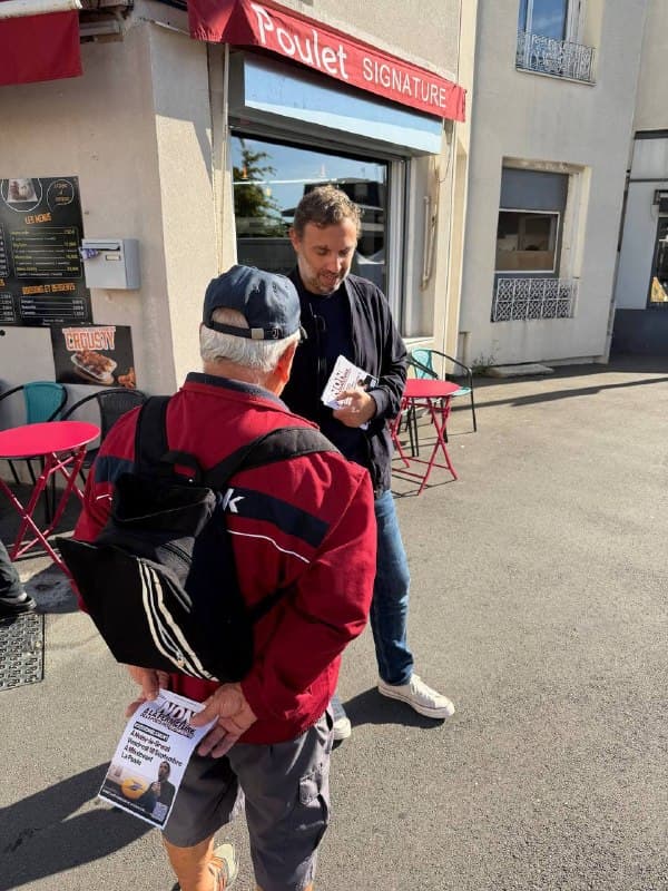 Un homme en veste sombre discute avec un passant en blouson rouge devant un commerce.