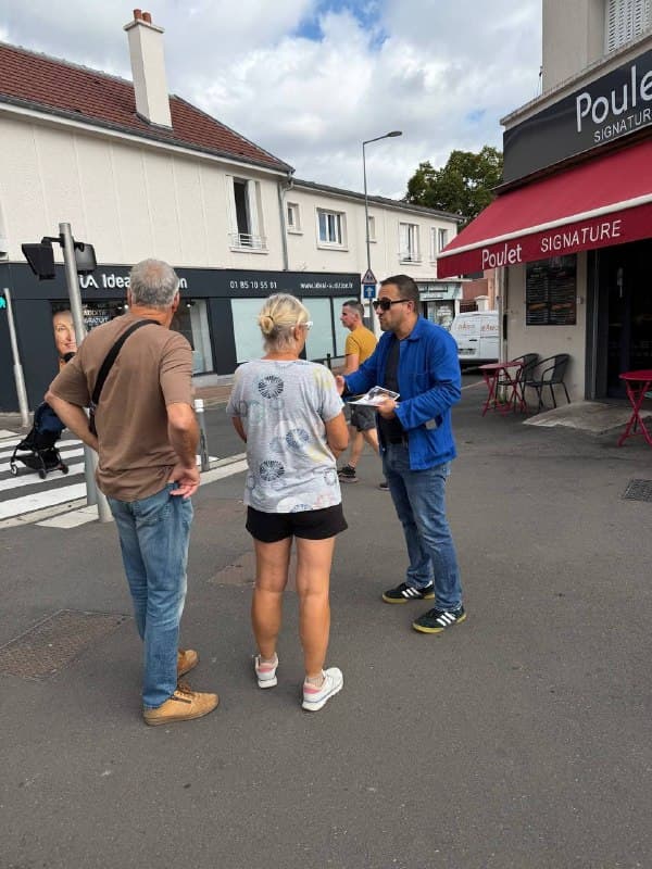 Un militant en veste bleue parle à deux passants à un carrefour.