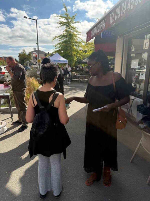 Une militante tend un tract à une passante devant des commerces.