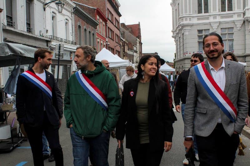 Quatre personnes, dont trois élus en écharpe tricolore, marchent dans une braderie entre les stands.
