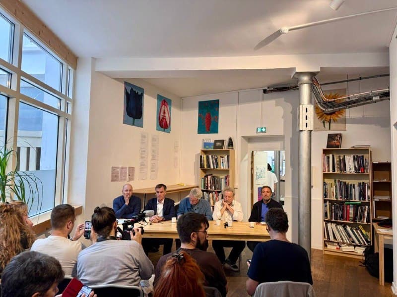 Une réunion publique dans une salle aux murs couverts de rayonnages de livres : cinq intervenants assis à une table font face au public.