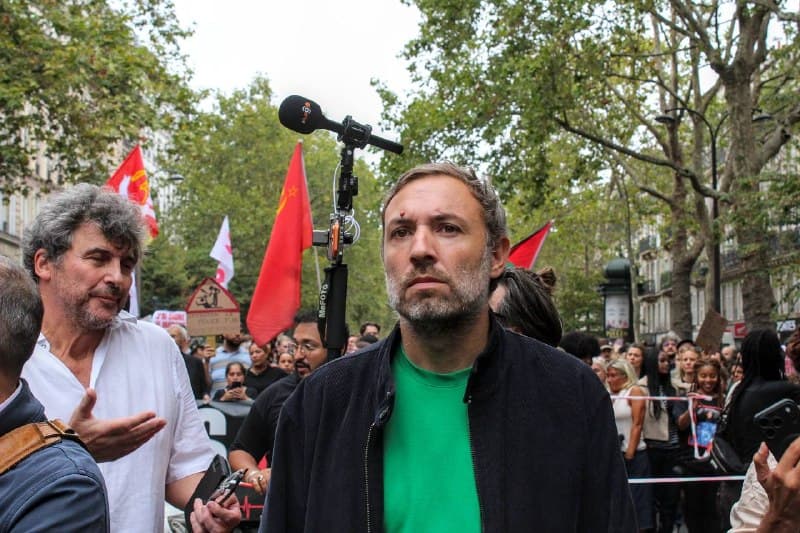 Un homme au tee-shirt vert, perche de micro au-dessus de lui, au milieu du cortège.