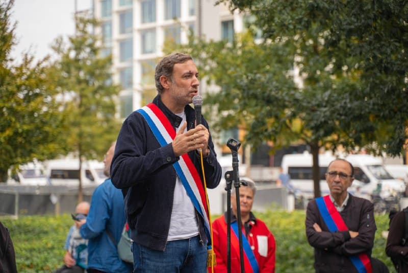 Thomas Portes, en écharpe tricolore, parle au micro lors d'un rassemblement en plein air.