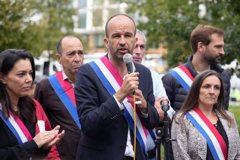 Un élu en écharpe tricolore parle au micro, entouré d'autres élus ceints de leur écharpe.