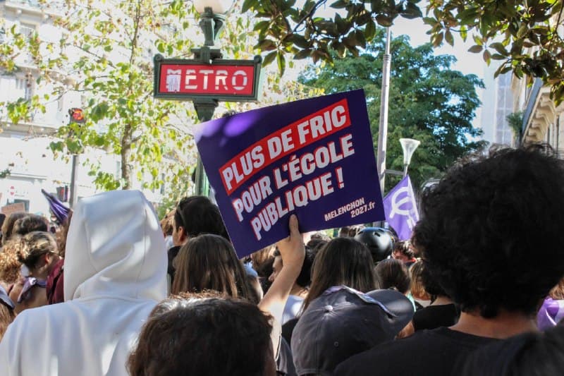Une pancarte violette « Plus de fric pour l’école publique ! » est brandie près d’une entrée de métro.