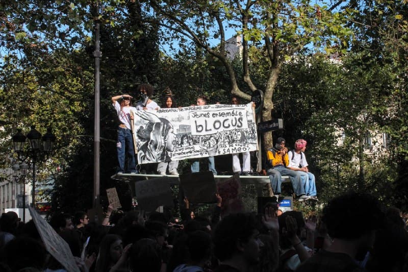 Des manifestants sur une estrade tiennent une banderole « Jeunes ensemble, blocus » au-dessus de la foule.