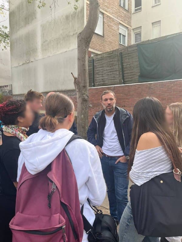 Thomas Portes échange avec des jeunes devant un mur ; deux jeunes femmes sont vues de dos au premier plan.