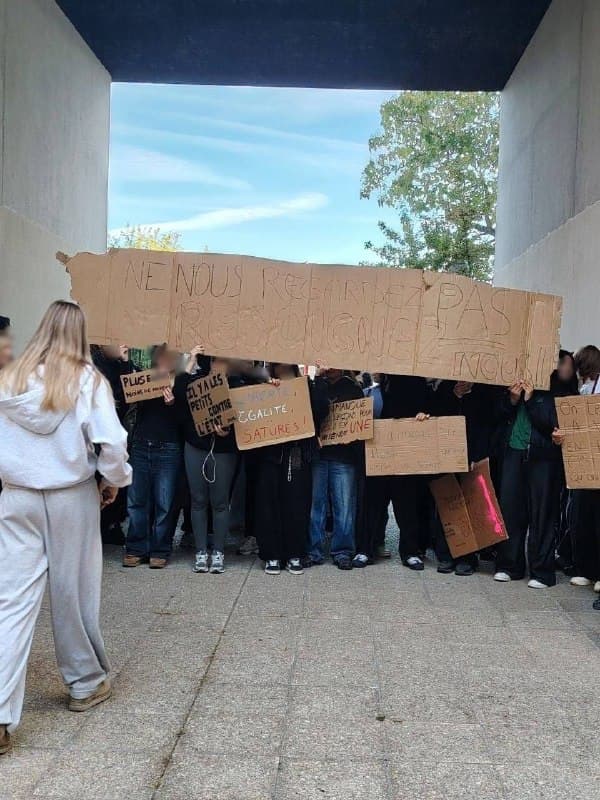 Des jeunes tiennent des pancartes en carton sous un passage couvert.