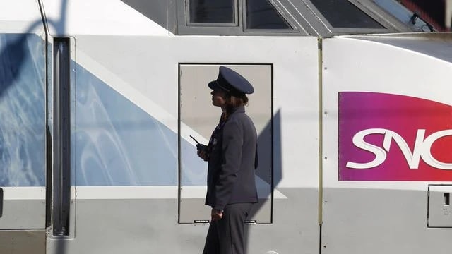 Un agent en uniforme et casquette marche le long d’une rame TGV portant le logo SNCF.