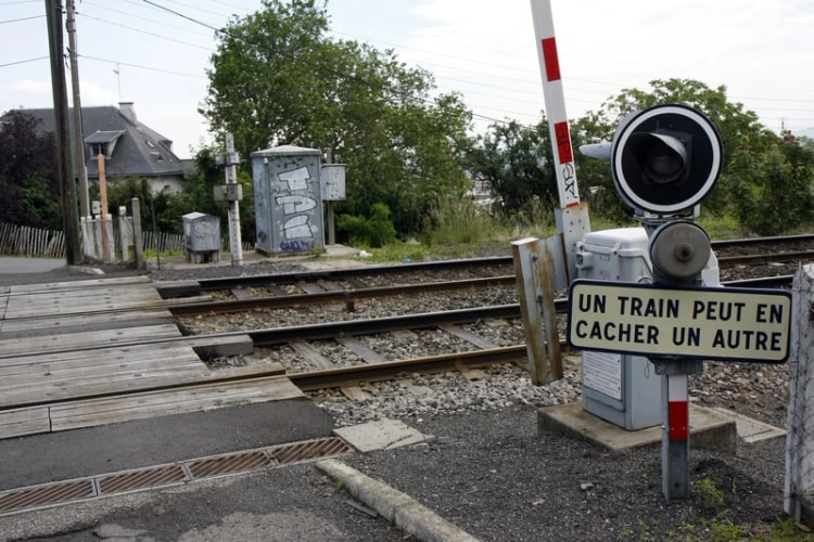 Passage à niveau de campagne avec sa barrière et un panneau « Un train peut en cacher un autre ».