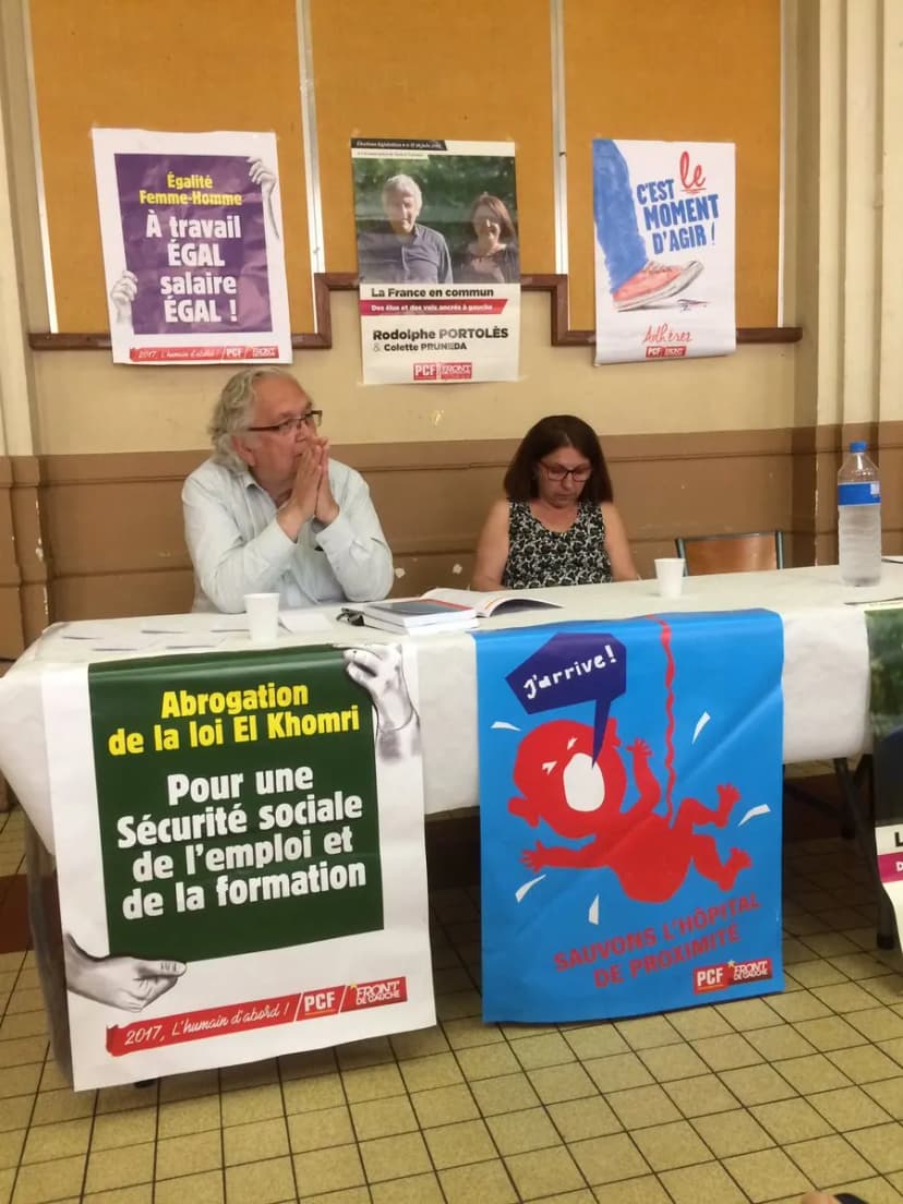 Homme et femme à une table de réunion, devant des affiches PCF et Front de gauche dont « Sauvons l'hôpital de proximité »