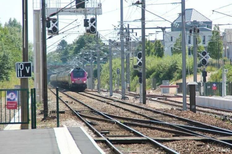 Train de marchandises tiré par une locomotive rouge sur des voies électrifiées, filigrane « © 78actu »