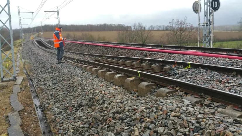 Un agent en gilet orange marche le long d’une voie ferrée dont un rail est marqué de peinture rouge.