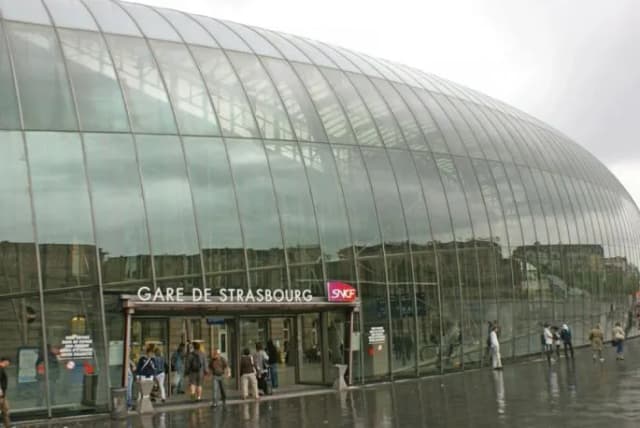 Façade de verre de la gare de Strasbourg un jour de pluie, quelques passants devant l’entrée.