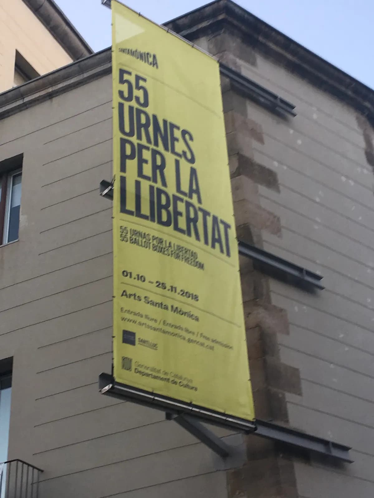 Bannière jaune sur une façade : « 55 urnes per la llibertat », exposition à Arts Santa Mònica du 01.10 au 25.11.2018