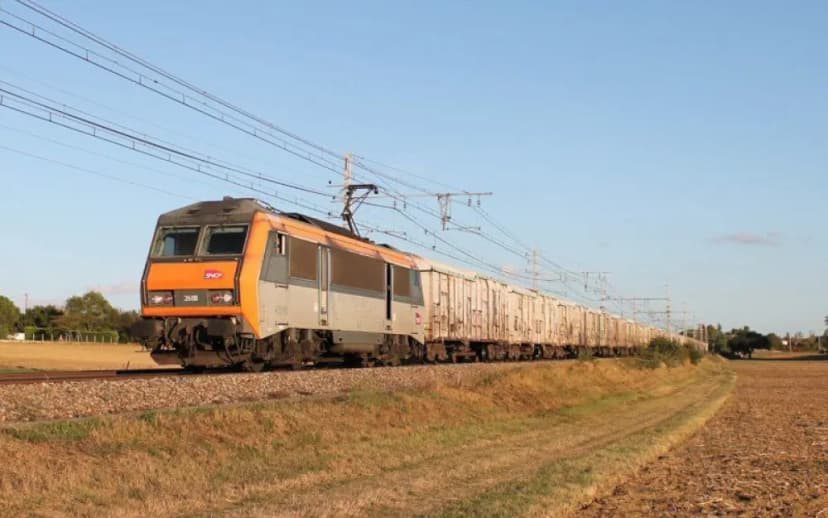 Locomotive orange et grise en tête d’un train de marchandises traversant la campagne.