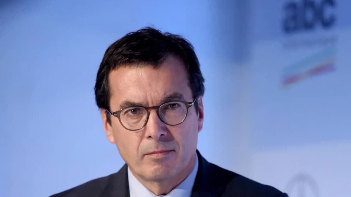 Photographie en gros plan d'un homme à lunettes en costume sombre, devant un fond bleu flou portant un logo « abc ».