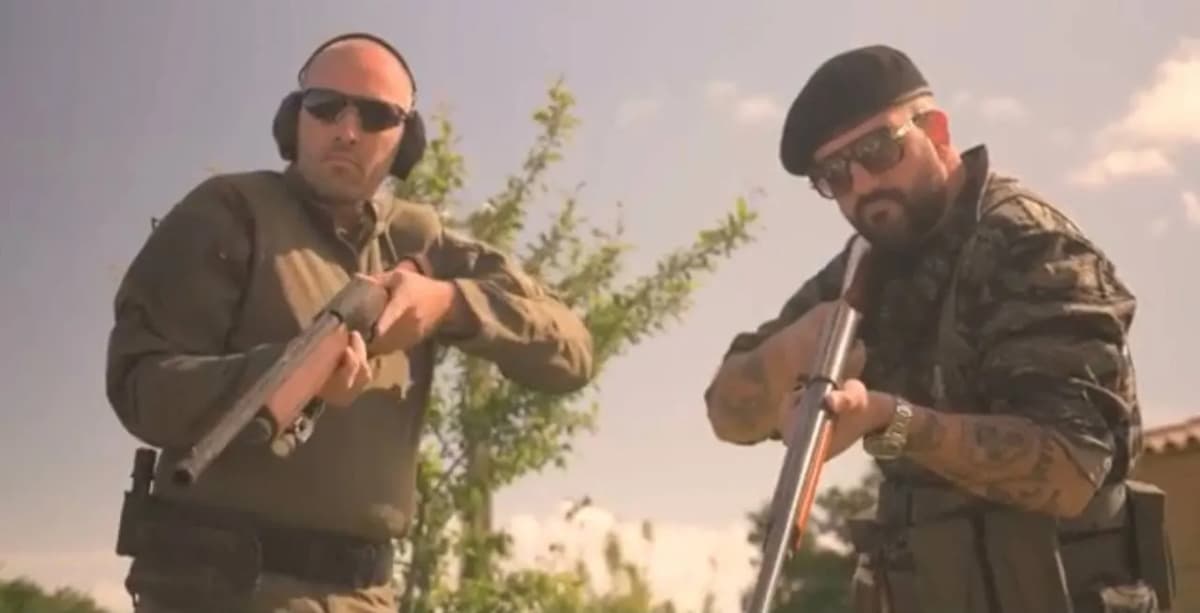 Deux hommes en tenue kaki et lunettes de soleil, l’un avec un casque antibruit, l’autre un béret, tiennent chacun un fusil.