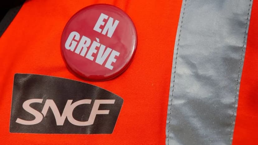 Badge rouge « En grève » épinglé sur un gilet orange portant un autocollant SNCF.