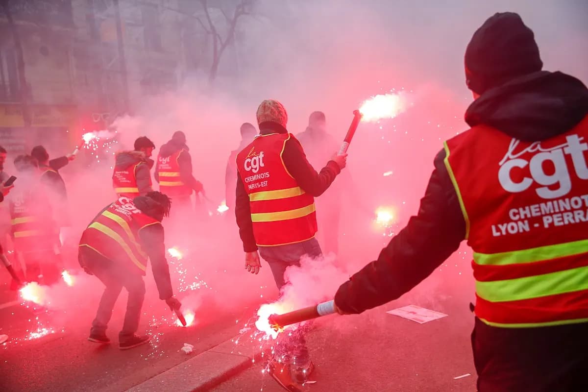 Manifestants en gilet rouge de la CGT cheminots « Lyon-Perrache » avec des fumigènes allumés, dans une fumée rouge.
