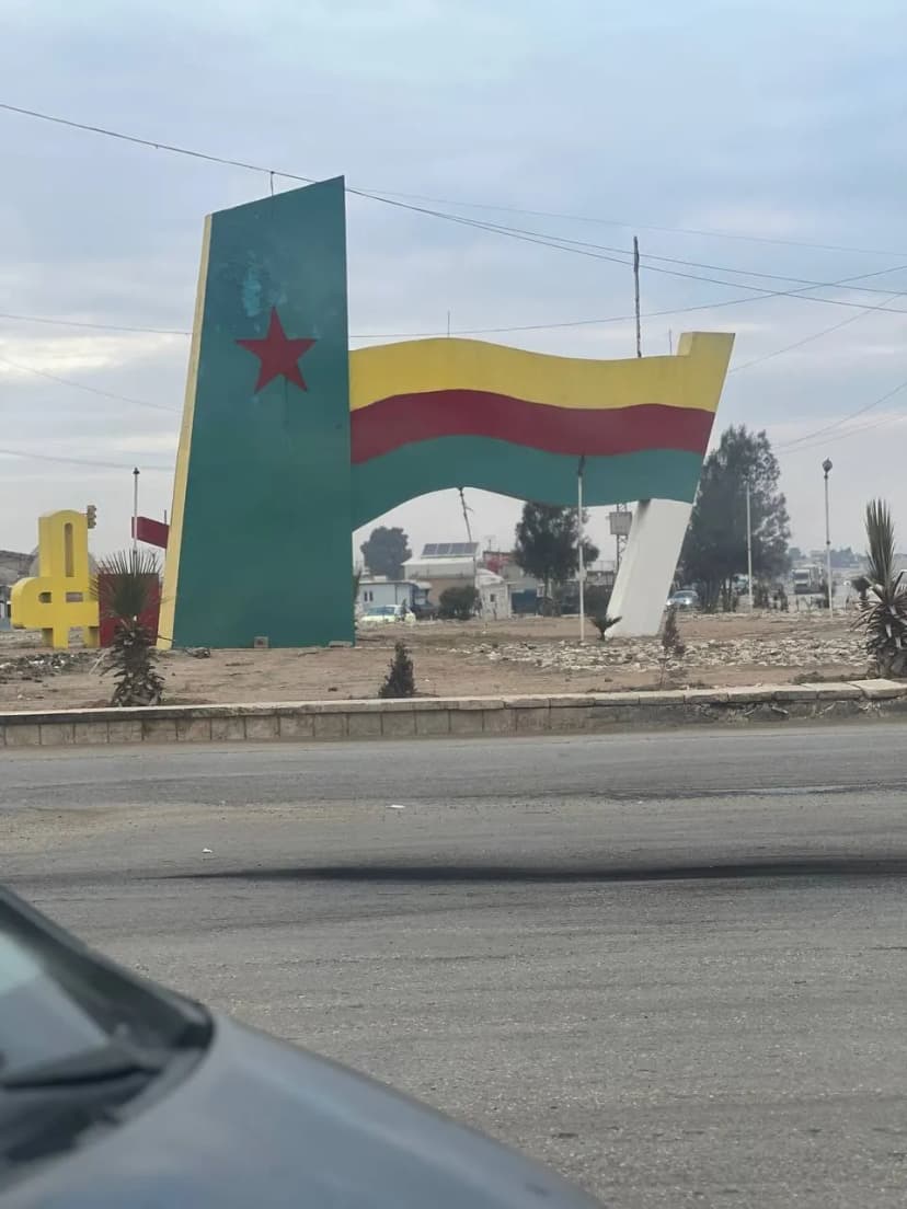 Monument de rond-point figurant un drapeau peint, vu depuis une voiture à l’arrêt.
