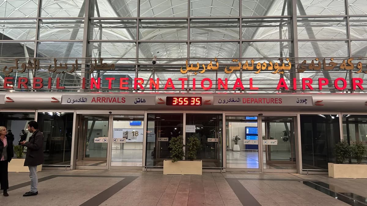 Façade vitrée d’un aéroport international, enseignes en arabe, kurde et anglais au-dessus des portes.