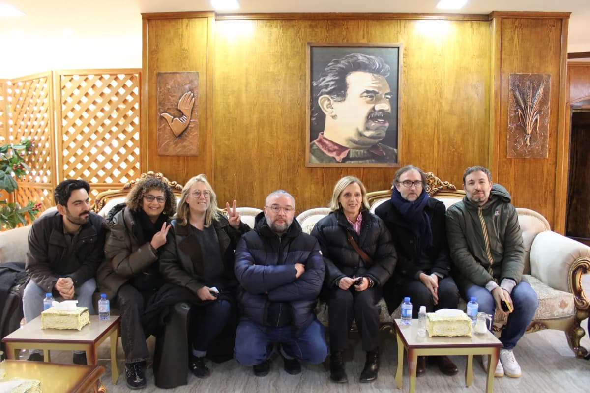 Sept personnes assises côte à côte sur un canapé, sous un portrait peint accroché au mur.
