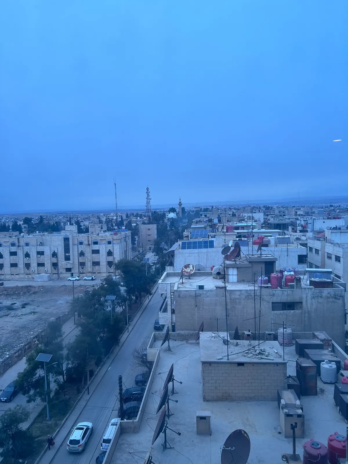 Vue d’une ville depuis un toit au petit jour, terrasses, paraboles et minaret au loin.