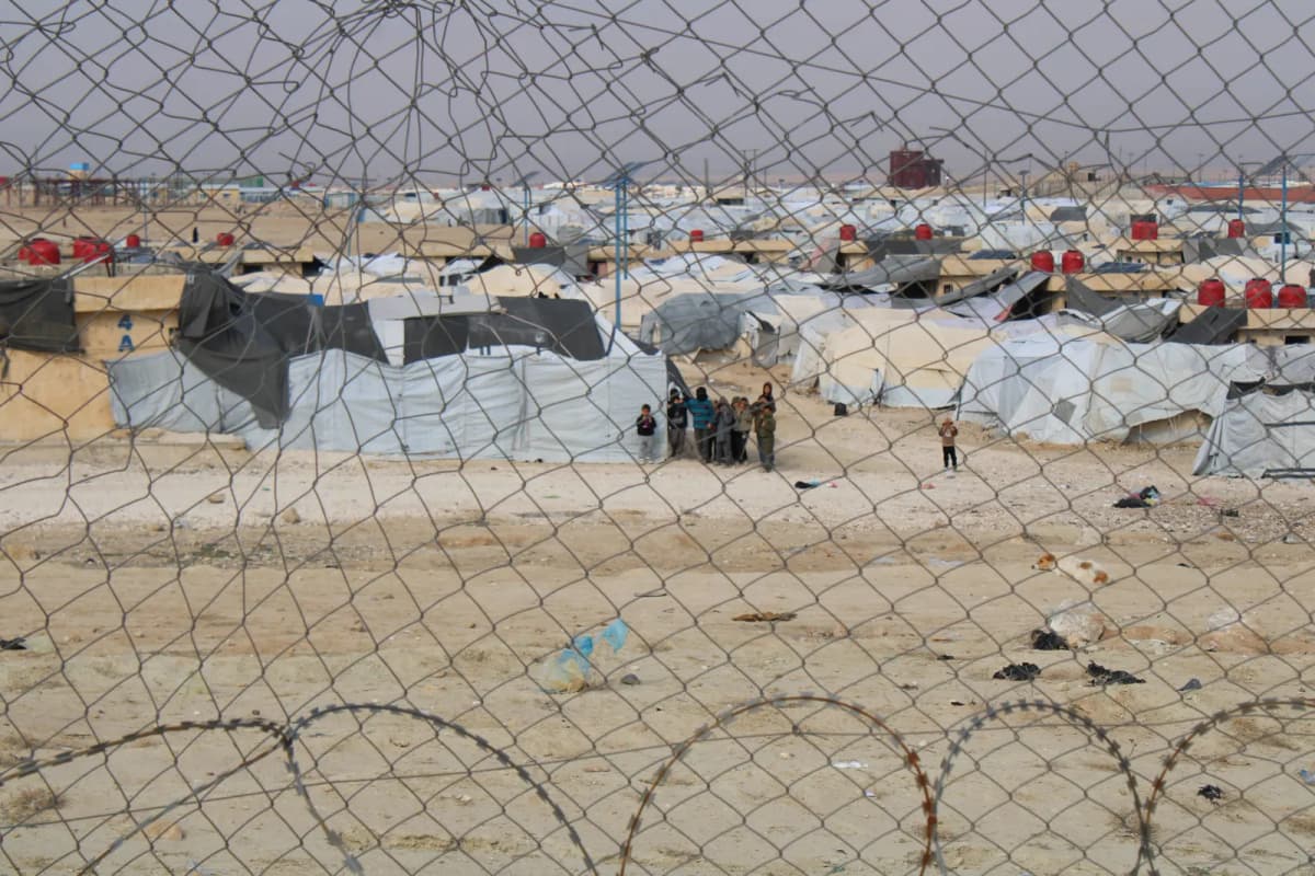 Camp de tentes s’étendant jusqu’à l’horizon, photographié à travers un grillage surmonté de barbelés.