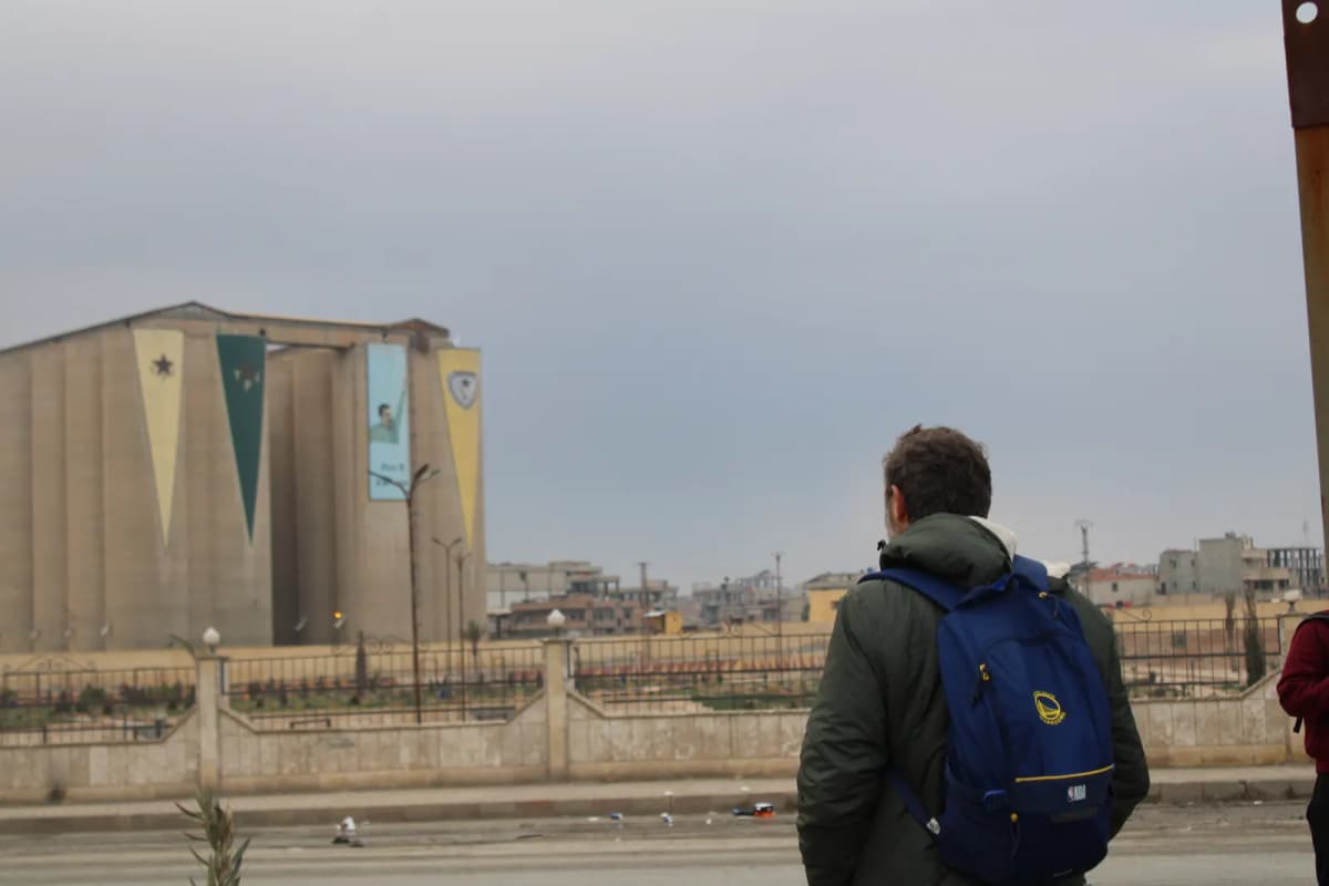 Un homme de dos regarde des silos de béton peints de fresques, dans une zone en ruines.