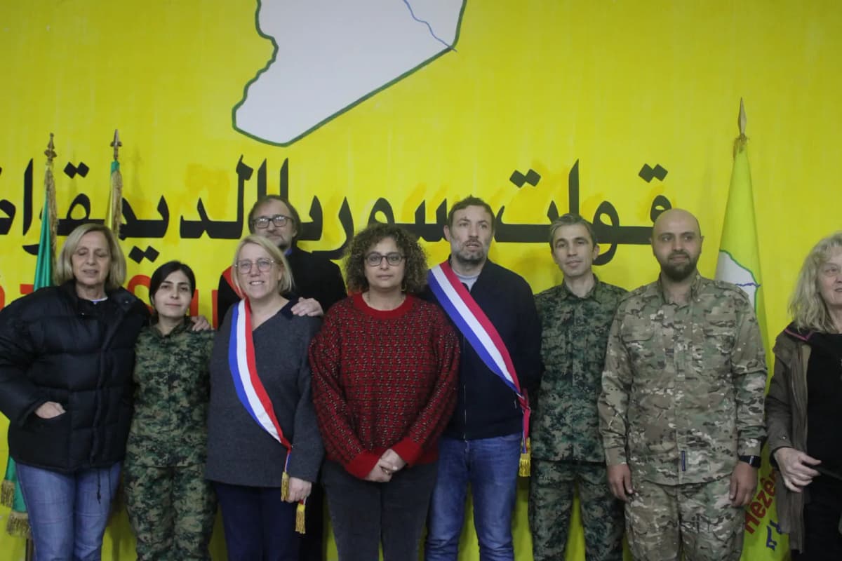 Groupe devant une banderole jaune : plusieurs personnes en écharpe tricolore aux côtés de personnes en tenue militaire.
