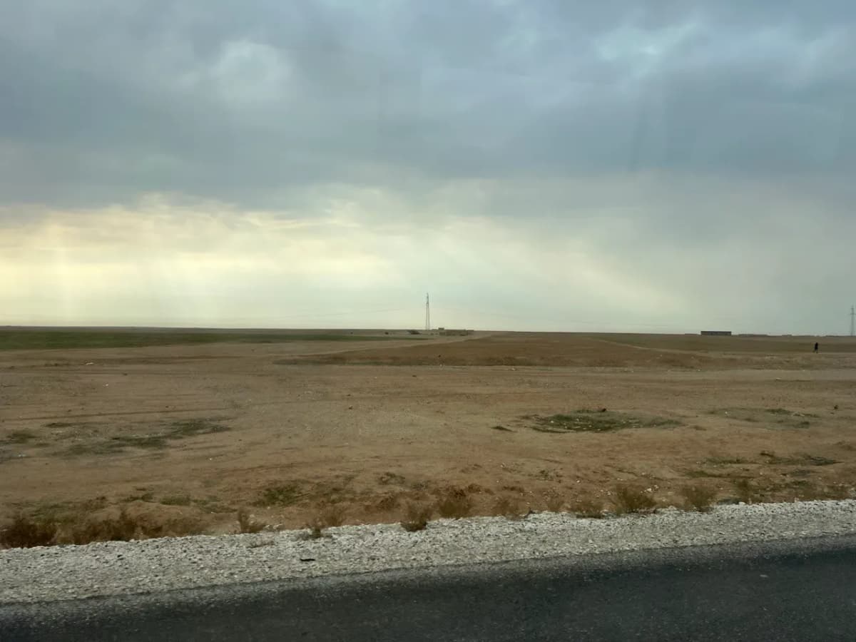 Plaine désertique sous un ciel couvert, vue depuis le bord d’une route.