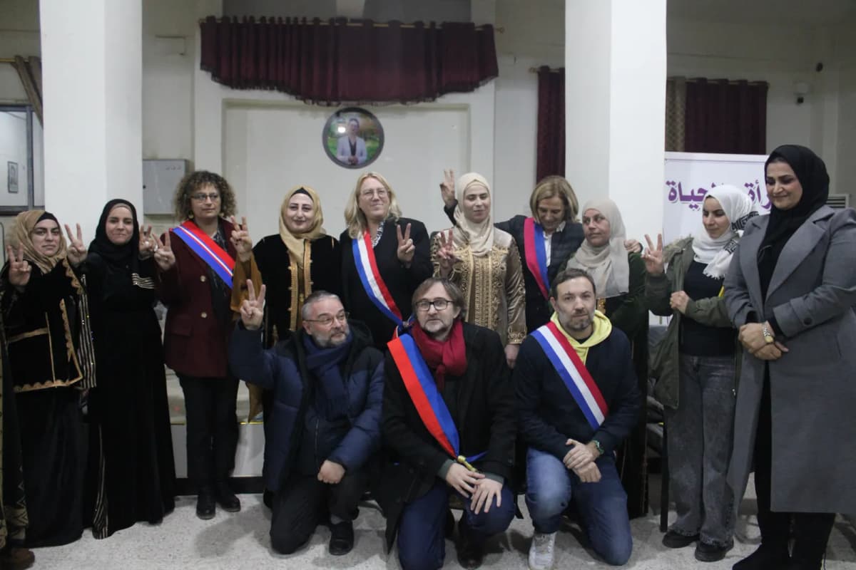 Une quinzaine de personnes en salle de réunion, dont des élus en écharpe tricolore ; plusieurs font le signe de la victoire.