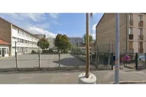 Capture d’une vue de rue montrant un bâtiment scolaire derrière une grille et une cour, à côté d’un immeuble.