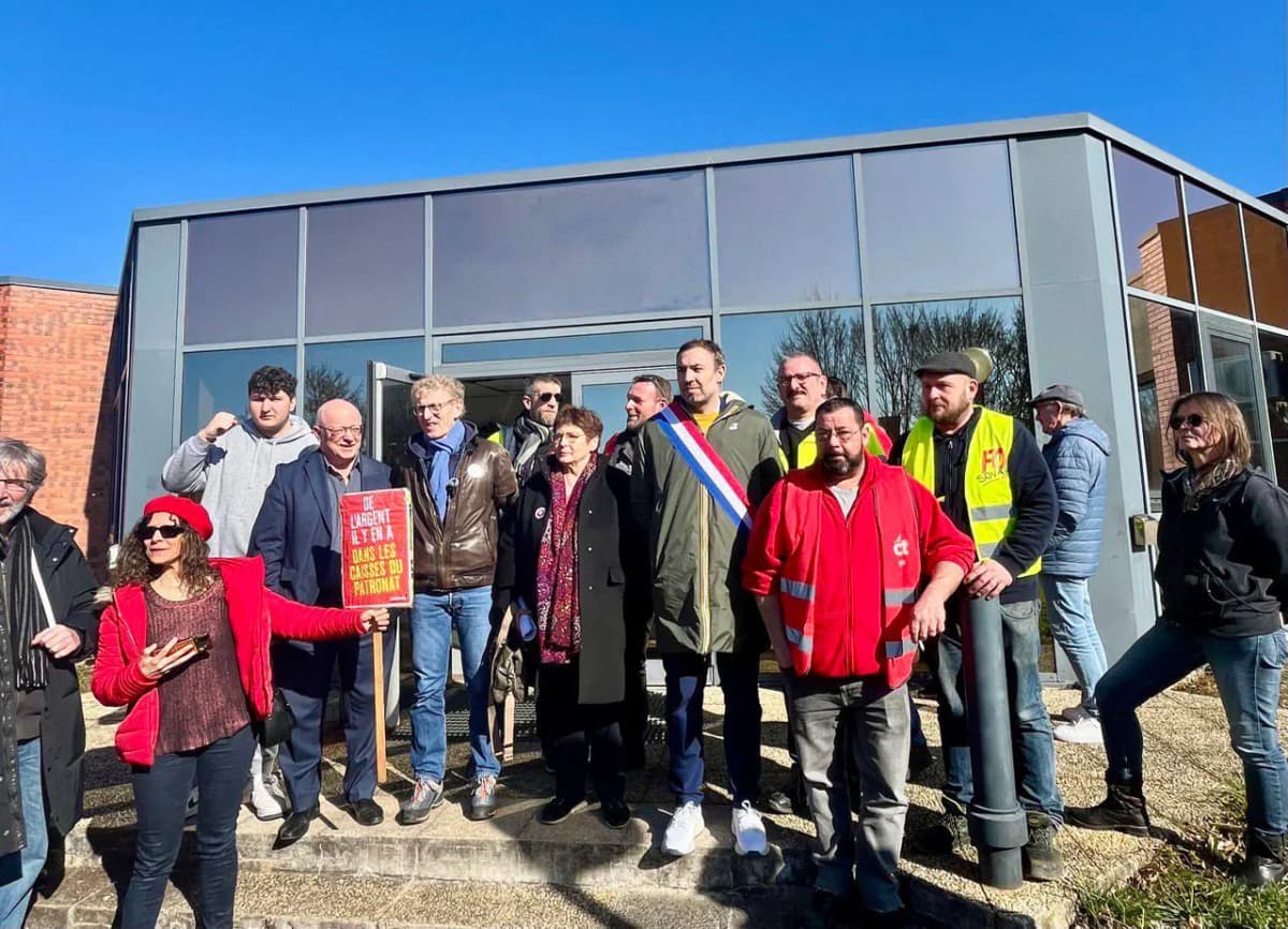 Groupe devant un bâtiment de bureaux avec une pancarte rouge, plusieurs en chasuble syndicale, une en écharpe tricolore.