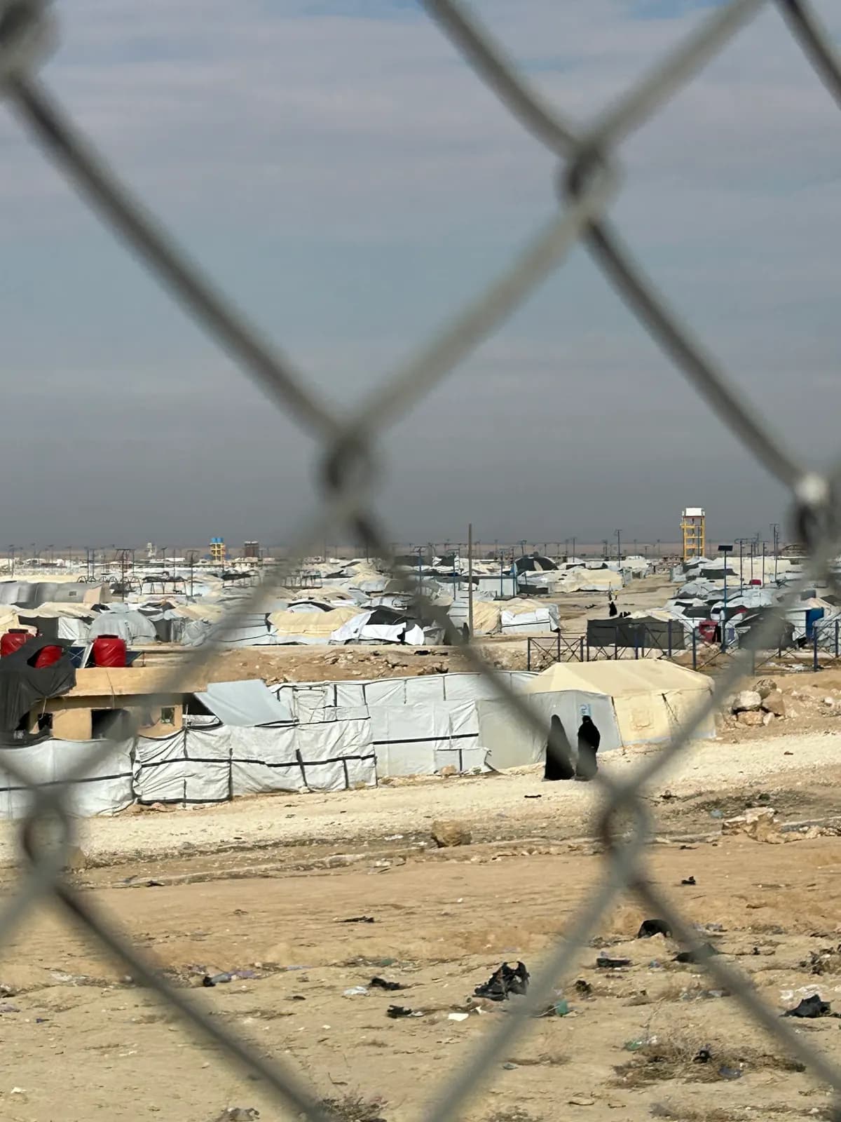 Camp de tentes s’étendant dans le désert, photographié à travers les mailles d’un grillage.