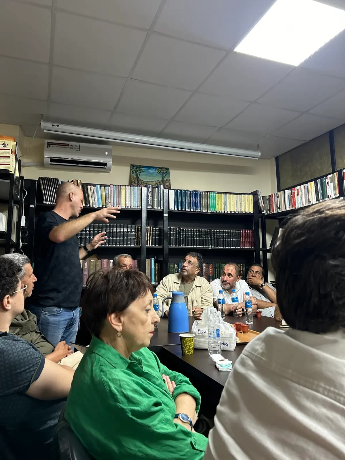 Réunion dans une salle bordée de rayonnages de livres, un intervenant debout s’adressant à l’assistance.