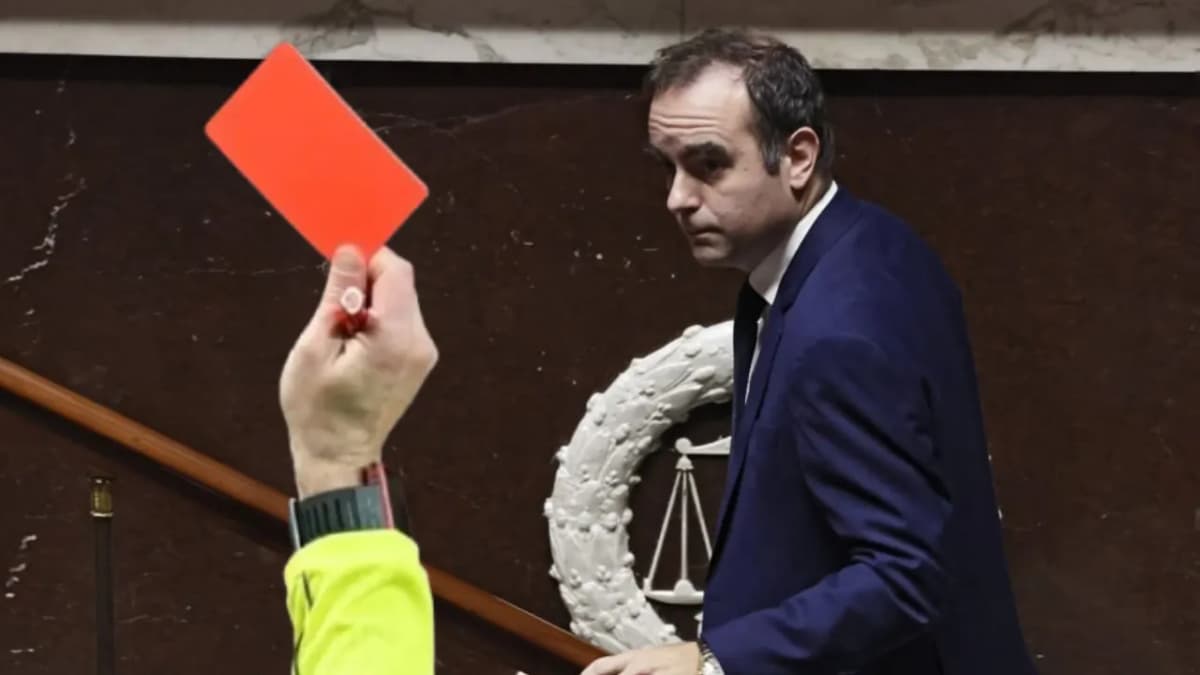 Photographie d’une main tenant un carton rouge au premier plan, face à un homme en costume qui se retourne dans l’hémicycle.