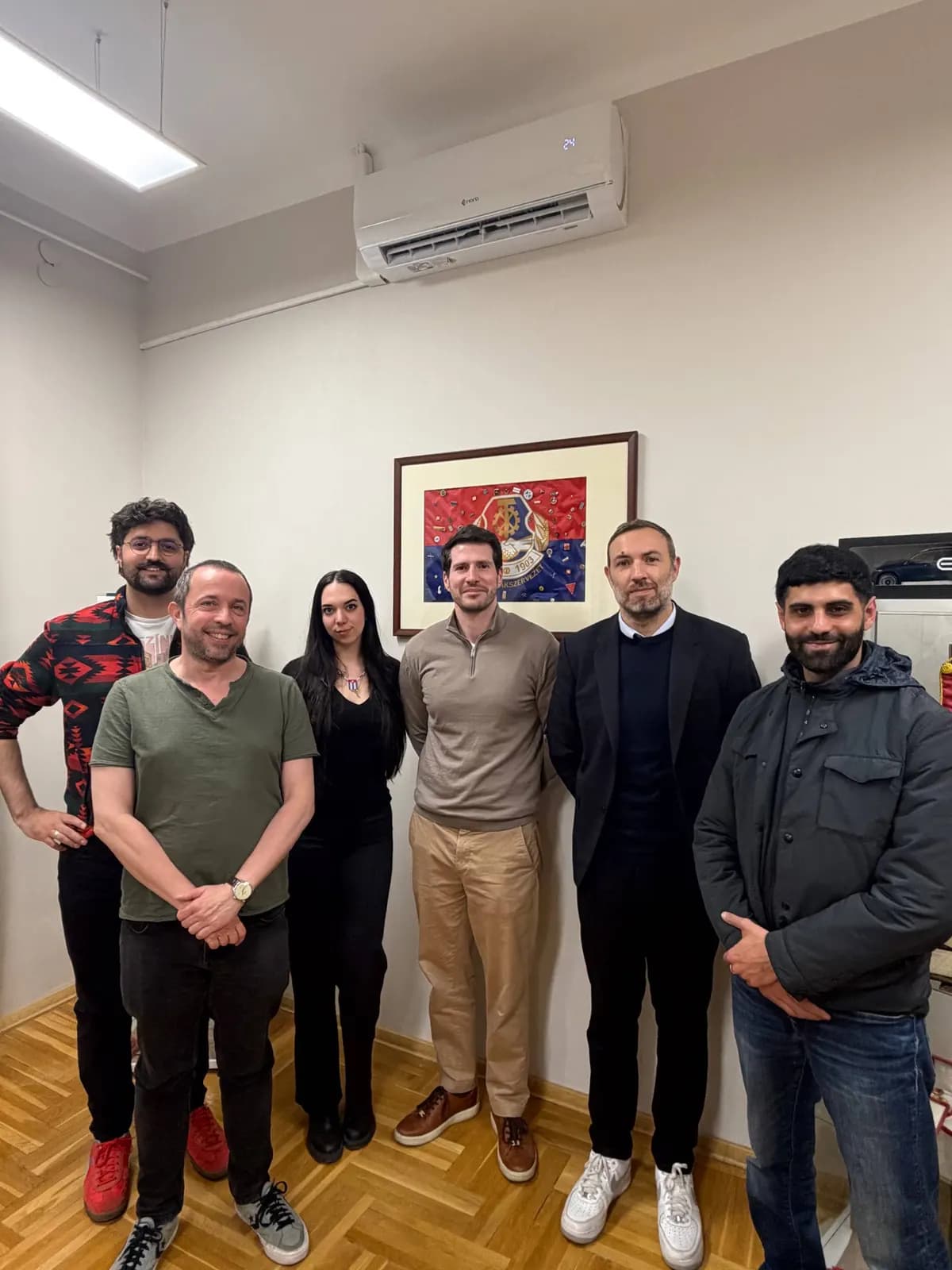 Six personnes posent dans un bureau, sous un tableau encadré.