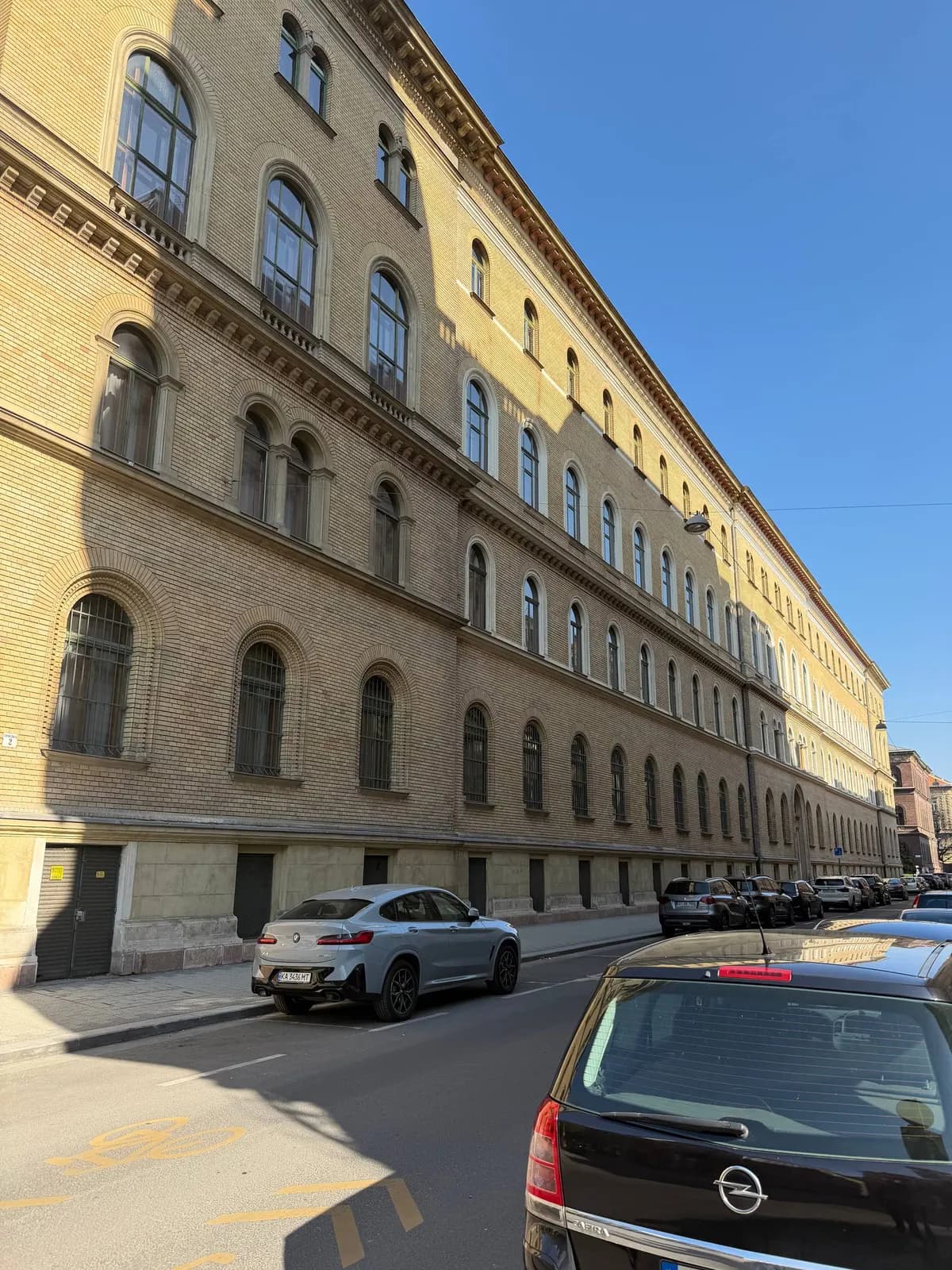Longue façade d’un bâtiment ancien bordant une rue en pente, voitures stationnées au pied.