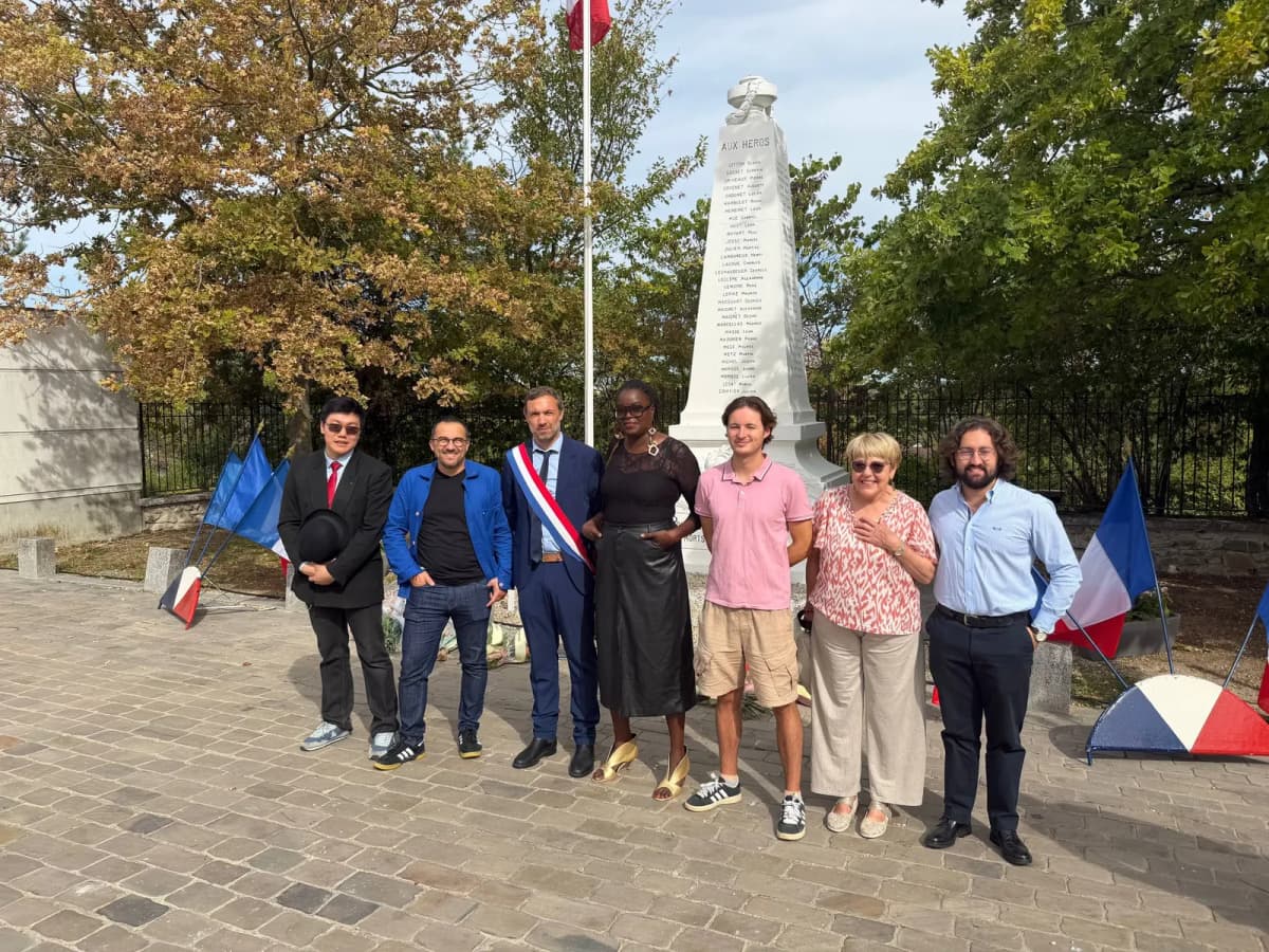 Sept personnes posent devant un monument aux morts, dont deux portent l’écharpe tricolore.