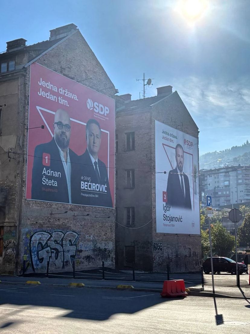 Deux pignons d’immeubles couverts d’affiches électorales du SDP, au soleil, au-dessus d’un mur tagué.