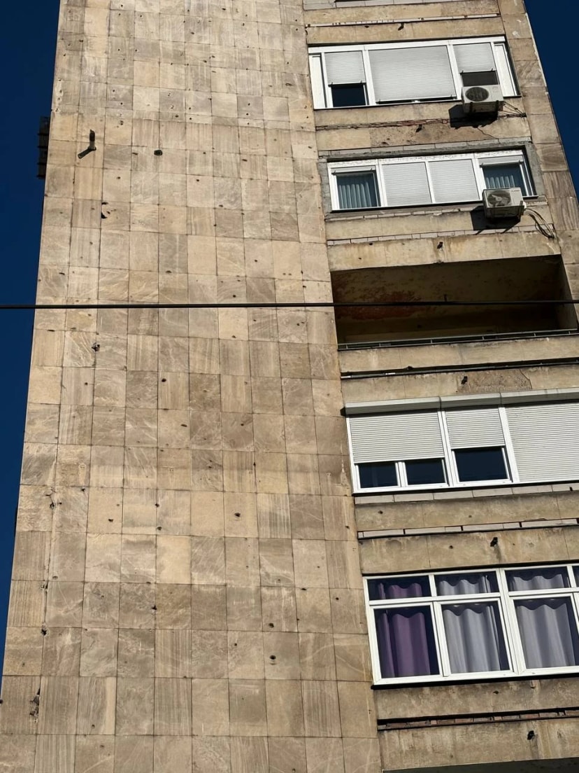 La façade d’un immeuble en pierre criblée d’impacts, avec des fenêtres et des climatiseurs.